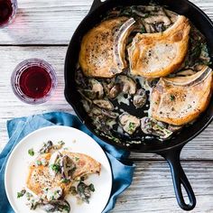 a skillet filled with meat and mushrooms on top of a wooden table next to a glass of wine