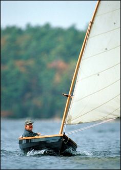 a man riding on the back of a sailboat in the water with trees in the background