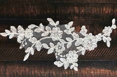 a white lace with flowers is on a wooden surface and it looks like an applique