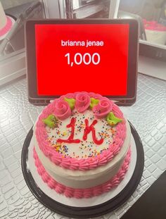 a birthday cake with pink frosting and sprinkles on top is displayed in front of a sign that reads 1, 000