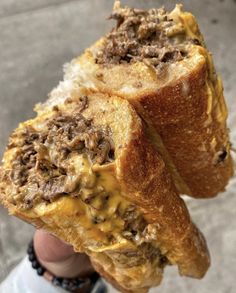 two pieces of bread with meat and cheese on them being held up by someone's hand