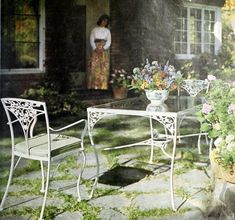 two white chairs and a table with flowers on it in front of a house next to a potted plant