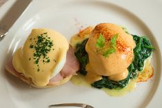 a white plate topped with an egg and ham covered in gravy next to a fork