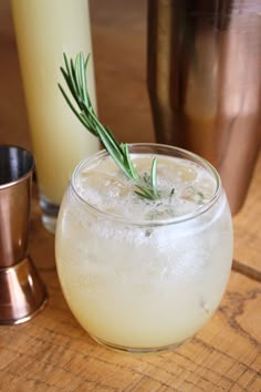 a drink in a glass with a rosemary sprig sticking out of it next to two glasses