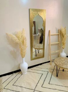 two vases with dry grass in front of a mirror on the wall next to a stool