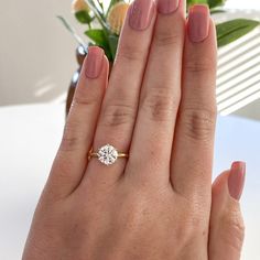 a woman's hand holding a diamond ring on her left hand, with flowers in the background