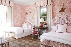 two beds in a room with pink wallpaper and white bedding, red accents