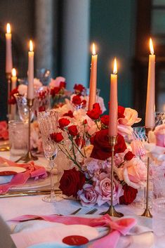 the table is set with candles and pink napkins on it, along with other place settings