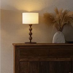 a lamp that is sitting on top of a wooden dresser next to a vase with grass in it