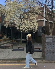 a woman walking down the street in front of a tree with white flowers on it