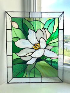 a stained glass window with a white flower on it's side and green leaves in the background