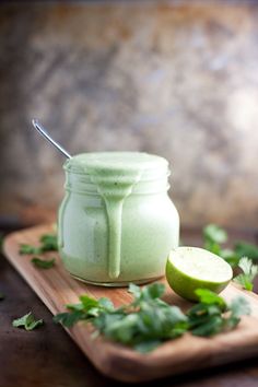 a jar filled with green liquid sitting on top of a cutting board next to an apple