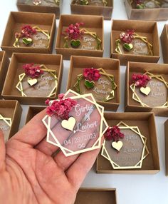 someone is holding their wedding favors in front of many small boxes with hearts and flowers on them