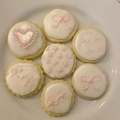 six decorated cookies on a white plate with pink bows and heart shaped frosting in the middle