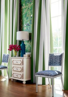 a room with green and white striped curtains, two blue chairs and a table with flowers on it