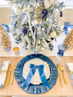 a blue and white christmas table setting with a tree in the backgrouf