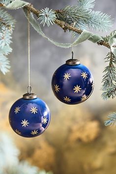 two blue christmas ornaments hanging from a tree