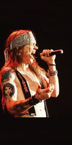 a man with long hair and tattoos on his arm holding a microphone in front of him