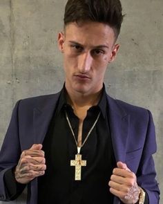 a man wearing a purple jacket and black shirt with a cross necklace on his chest