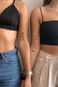 two women with matching tattoos on their arms and stomachs, both wearing crop tops