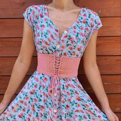 a woman wearing a dress with flowers on it and a pink belt around her waist