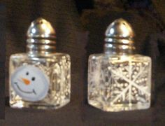 two glass salt and pepper shakers with a snowman on the front one is silver