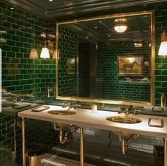 a green tiled bathroom with two sinks and mirrors on the wall, along with three lights