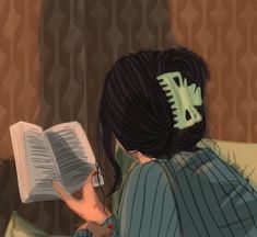 a woman reading a book while sitting on a couch with her hair in a bun