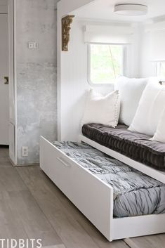 a white couch with pillows on it in front of a window and wooden flooring