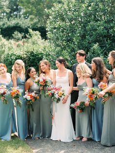 a group of women standing next to each other in front of trees and bushes holding bouquets