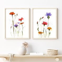 two paintings on the wall above a shelf with a vase and flowers in front of them