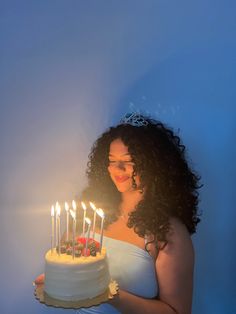 a woman holding a cake with lit candles on it in front of a blue background