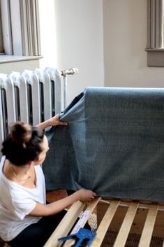 a woman sitting on the floor next to a bed frame