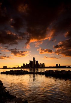 the sun is setting over a large body of water with some buildings in the background