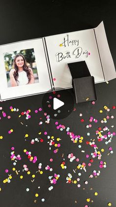 an open photo album with confetti on it and a happy birthday card next to it