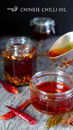 a wooden spoon pouring honey into a glass jar on top of a table next to chili peppers