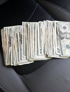 a bunch of money sitting on top of a black leather seat next to a pile of cash