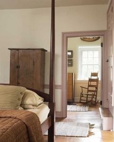 a bed sitting inside of a bedroom next to a wooden dresser and rocking chair on top of a hard wood floor