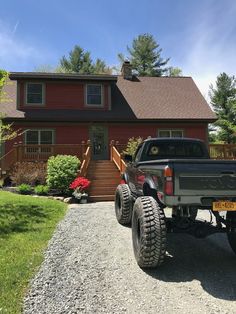 a black truck parked in front of a red house with large tires on it's flatbed