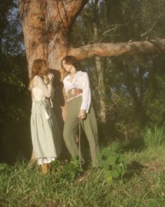 two people standing next to each other near a tree