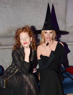 two women in black dresses and witches hats posing for the camera with their hands on their chins