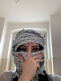 a woman wearing a scarf covering her face and making the v sign with her fingers