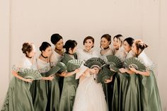 a group of women standing next to each other holding green hand fans in front of a white wall