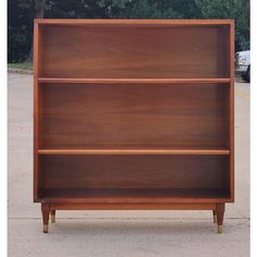 a wooden bookcase sitting on top of a sidewalk next to a parking lot with trees in the background