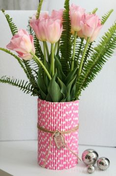 pink flowers are in a vase with green leaves and silver balls on the table next to it