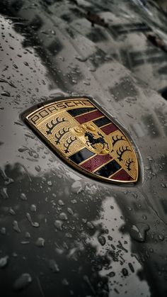 the front end of a porsche car with rain drops on it's hood and badge