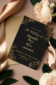 an elegant black and gold wedding card with flowers on the side, along with satin ribbons