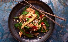 a metal bowl filled with vegetables and chopsticks on top of a blue table