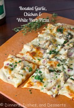 a pizza with chicken and white herb toppings on a cutting board next to a bottle of beer