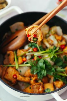 chopsticks holding up food in a pan with vegetables and meat on the side